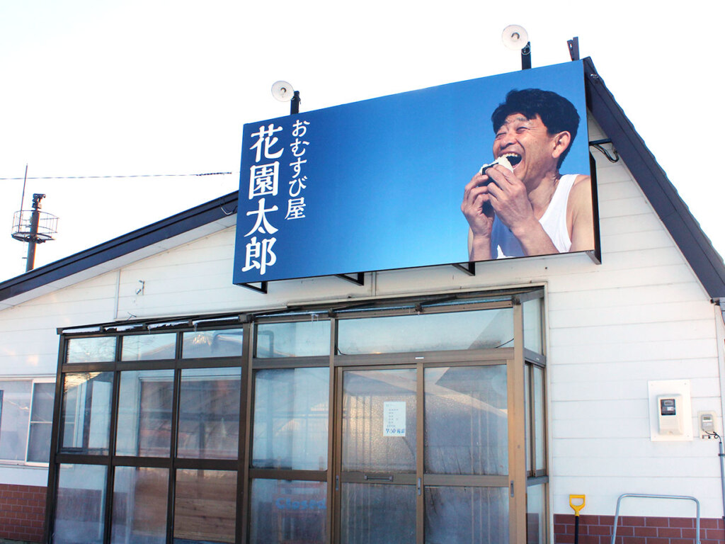 店主の佐藤さんが雪の中、満面の笑みで頬張る 圧倒的インパクトの看板。きっと脳裏に焼き付くはず(笑)