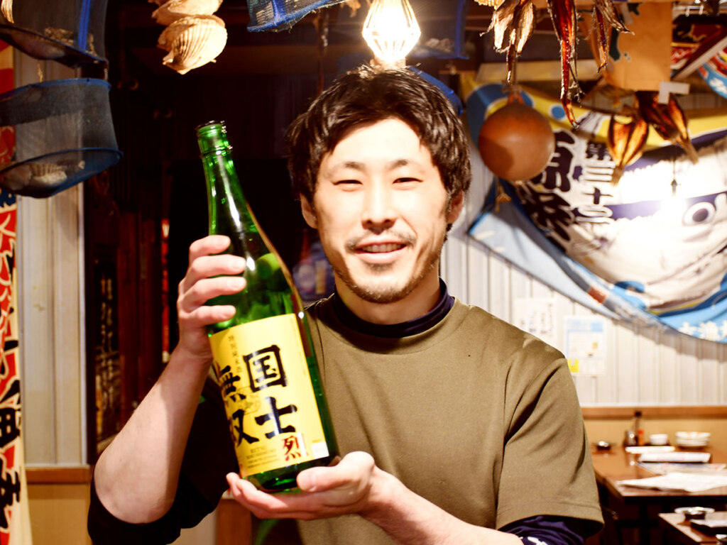 シリーズを考案した調理担当の藤吉さん。ほかメニューはカニミソを使った痛風豆腐やウニとイクラの痛風軍艦など、その名に恥じぬラインアップです。大漁旗が上がる活気溢れる店内で、全国各地の酒の肴にぜひ
